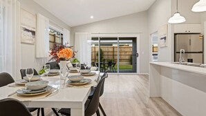A modern kitchen with a large island, sliding glass doors to a backyard, and a dining area with a table set for four. - Newly Built 4BR Family Oasis | Comfort & Space (Logan Reserve)