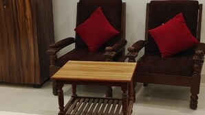 Two wooden armchairs with red cushions and a small wooden table in a room with a white wall and a wooden wardrobe. - RAGHAV STAY INN (Faizabad)