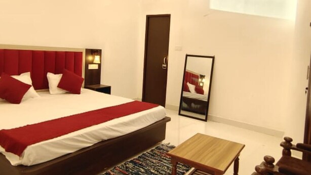 A hotel room with a large bed, a bedside table, a mirror, an air conditioning unit, and a window. - RAGHAV STAY INN (Faizabad)