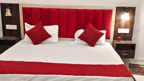 A bed with a red headboard, white bedding, and red and white pillows. There are two bedside tables with lamps and a small drawer. - RAGHAV STAY INN (Faizabad)
