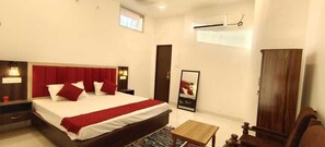A hotel room with a large bed, a bedside table, a nightstand, a wooden wardrobe, a mirror, and a small table. - RAGHAV STAY INN (Faizabad)