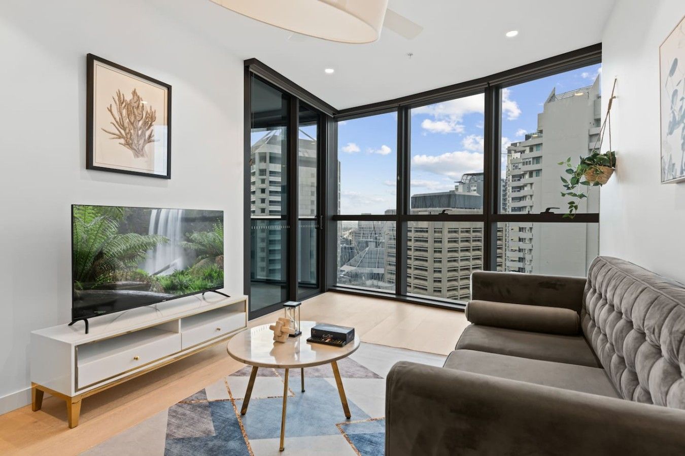 A modern living room with a large TV, a sofa, a coffee table, and a city view through large windows.