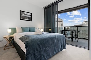 Ein modernes Hotelzimmer mit einem großen Bett, einem kleinen Tisch mit Stühlen, einem Balkon mit Tisch und Stühlen sowie einem gerahmten Bild an der Wand.