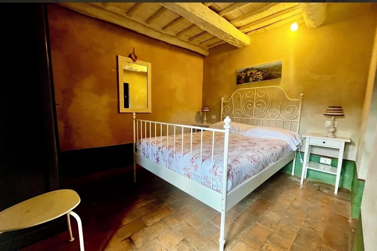A bedroom with a single bed, a bedside table, a chair, and a wall-mounted mirror.