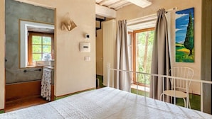 A bedroom with a bed, a window, a radiator, a chair, and a painting on the wall. - La Cervaiola  (Porano)