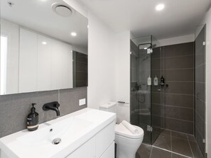 Un baño moderno con un lavamanos blanco, un inodoro y una zona de ducha con mampara de vidrio.