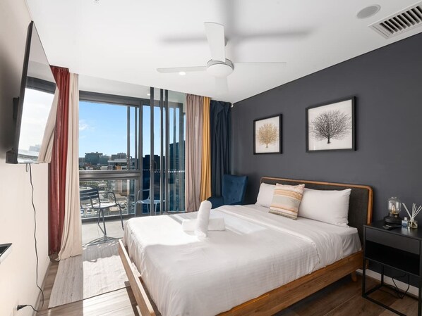 Un dormitorio moderno con una cama grande, ventilador de techo, vistas de la ciudad y un balcón con cortinas.
