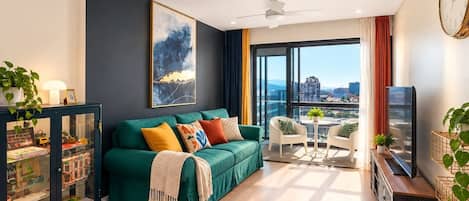 A modern living room with a green sofa, a glass cabinet, a television, and a city view.