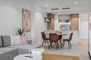 A modern living room with a grey sofa, a coffee table, and a dining area with a round table and chairs.