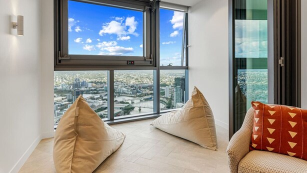 A modern living room with large windows offering a city view, two bean bags, and a sofa with patterned cushions.