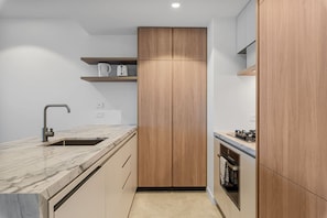 A modern kitchen with a marble countertop, a sink, wooden cabinets, and a built-in oven.