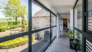 A corridor with large windows, a stone wall, and a view of a rural landscape. - New: Le Havre du Py, 230m² nestled in the heart of the fields (Compolibat)