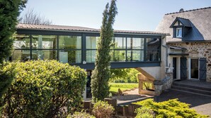 A modern house with a glass bridge connecting two sections, surrounded by lush greenery. - New: Le Havre du Py, 230m² nestled in the heart of the fields (Compolibat)