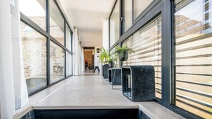 A modern hallway with large windows, stone walls, and black planters with green plants. - New: Le Havre du Py, 230m² nestled in the heart of the fields (Compolibat)