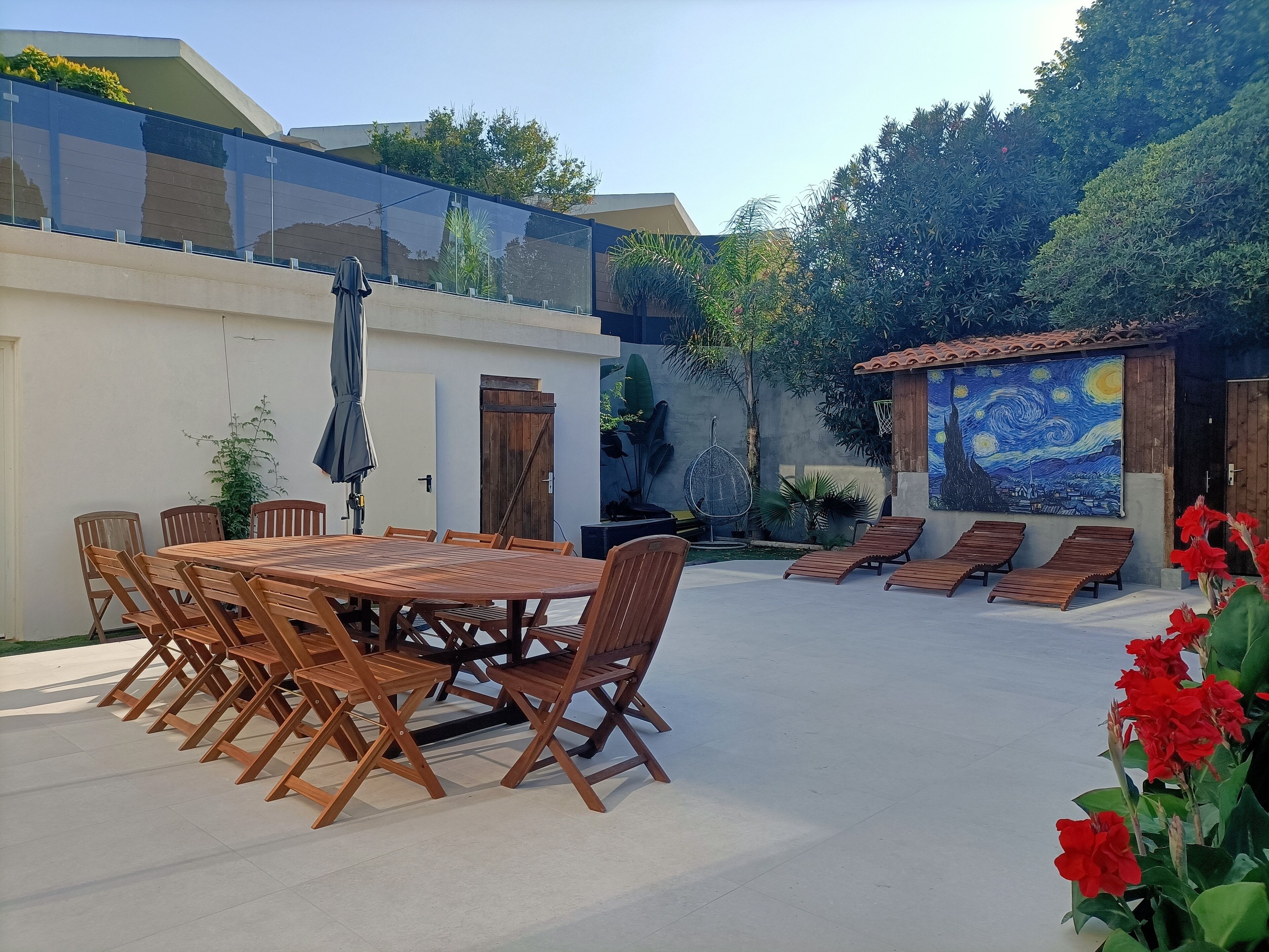 Un patio al aire libre con una mesa y sillas de madera, una silla colgante y un mural en la pared.