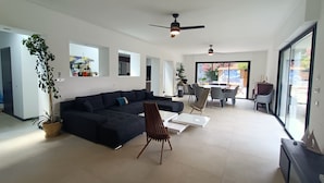 A modern living room with a dark-colored sectional sofa, a wooden chair, and a dining area with a table and chairs.