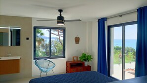 A bedroom with a large window, a bed, a chair, a dresser, and a ceiling fan.