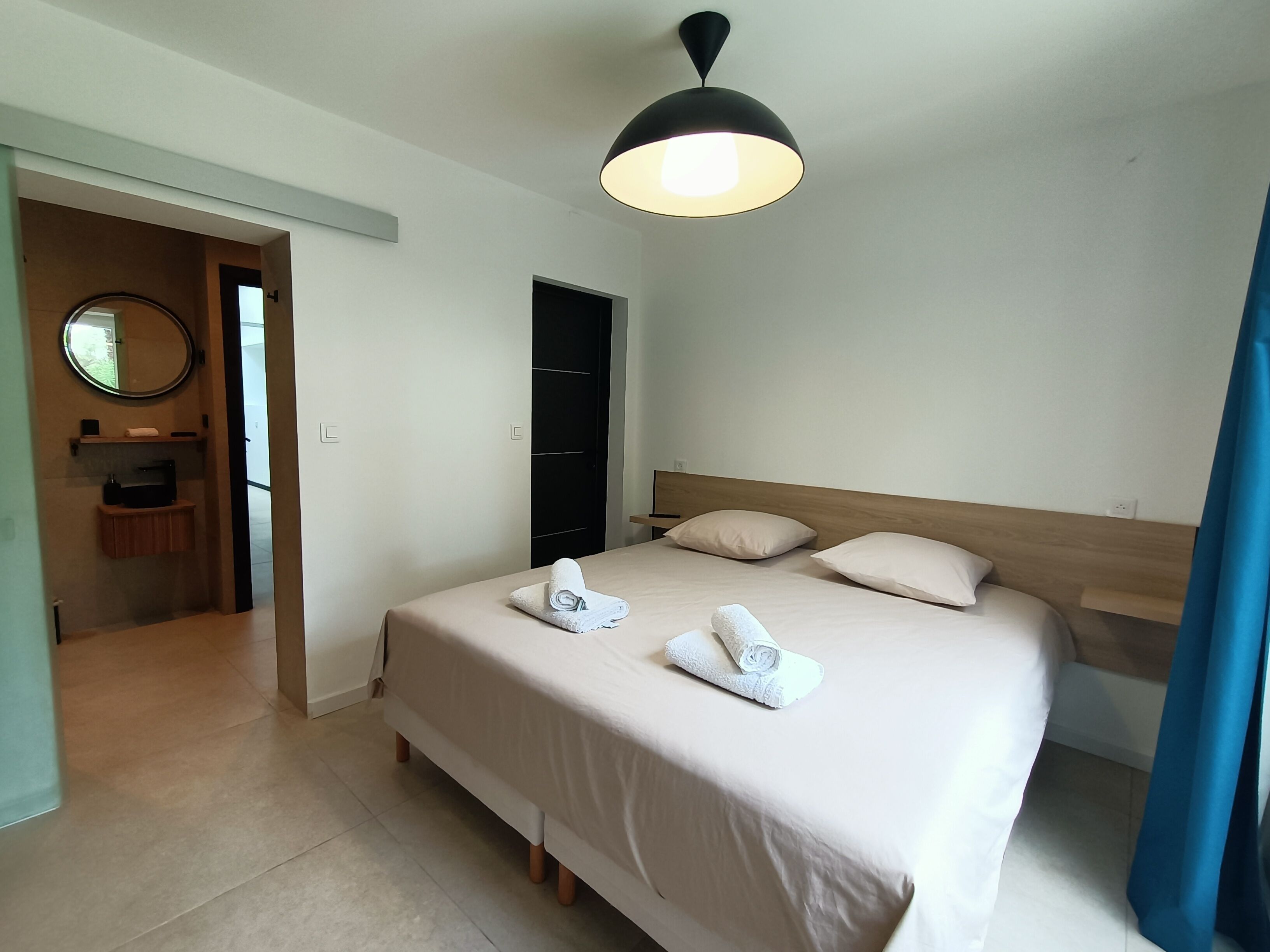 A hotel room with a bed, a bedside table, a mirror, and a door leading to a bathroom.