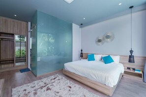 Ein modernes Schlafzimmer mit Glastrennwand, einem großen Bett mit weißer Bettwäsche und blauen Kissen sowie einem Holz-Kopfteil.