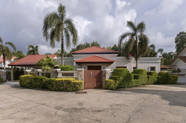 Un barrio residencial con casas de techos rojos, rodeado de setos cuidados y palmeras.
