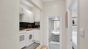 Une cuisine de taille réduite avec des meubles blancs, un lave-linge et un carrelage à motifs à carreaux.