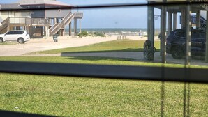 Uitzicht op een pand aan het strand, met een gazon, een houten terras en een gebouw met balkon.