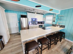 A kitchen with a large island, bar stools, a refrigerator, and a microwave.