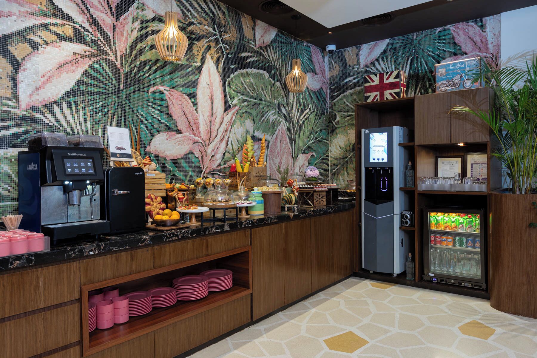 A hotel reception area with a coffee machine, a water dispenser, and a refrigerator stocked with beverages.