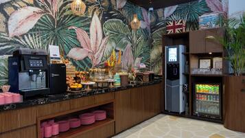 Ein Hotel-Rezeptionsbereich mit einer Kaffeemaschine, einem Wasserspender und einem mit Getränken gefüllten Kühlschrank.