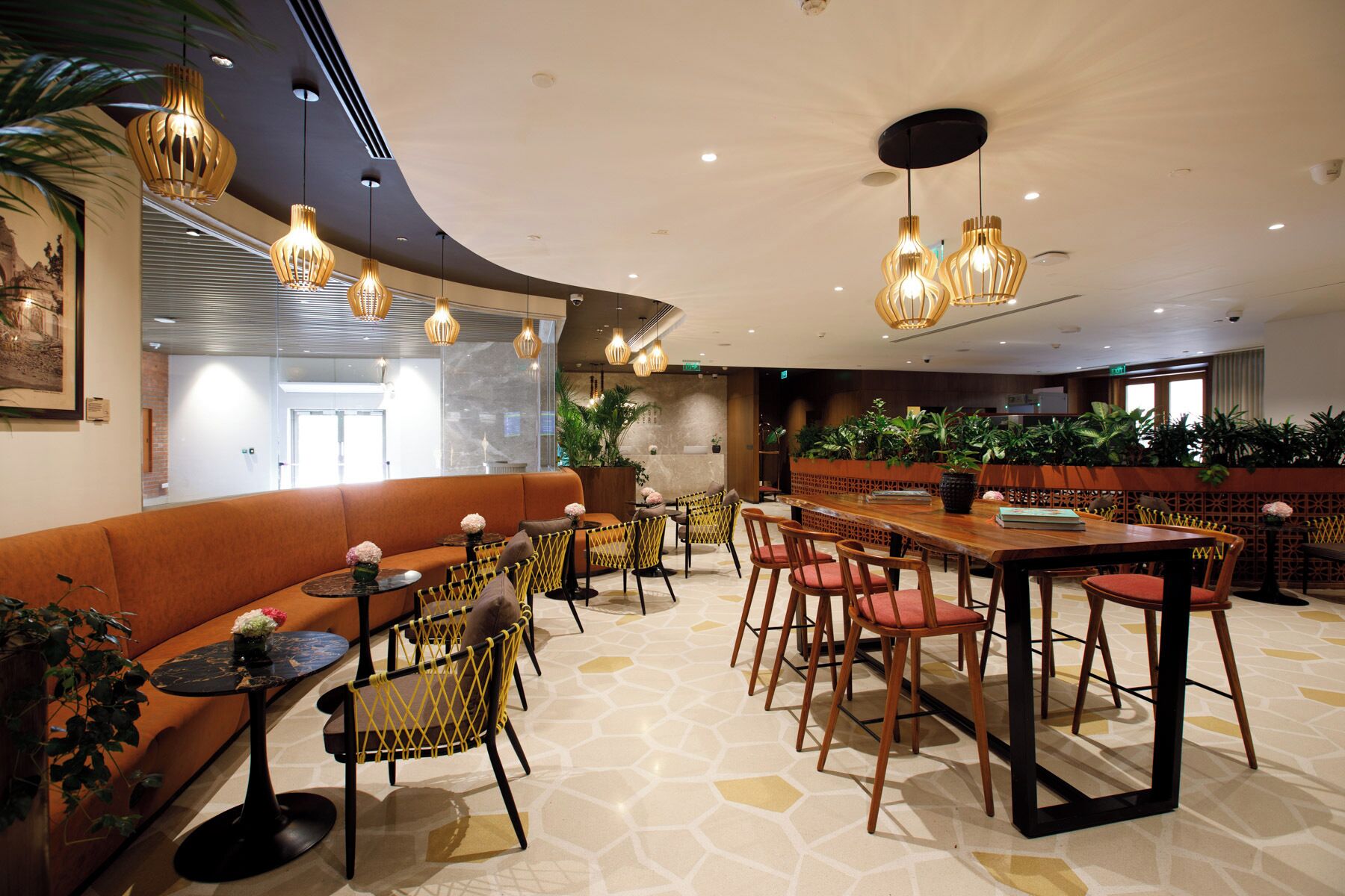 A modern interior with a curved ceiling, pendant lighting, a bar area, seating arrangements, and potted plants.