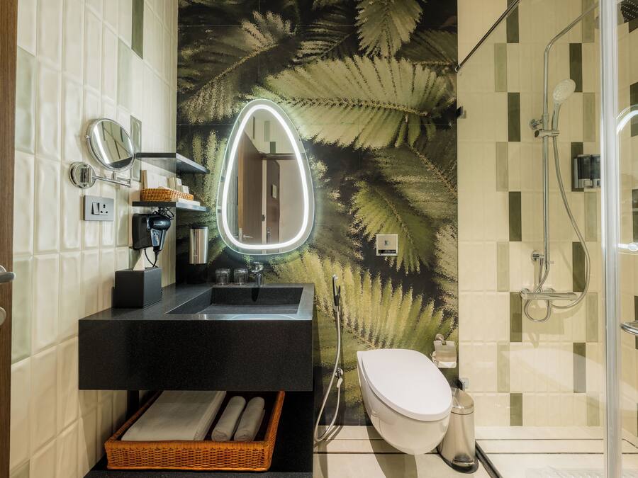 Un bagno moderno con un mobile lavabo nero, un WC bianco, box doccia in vetro e un murale con foglia di felce.