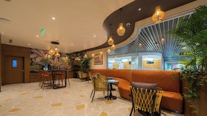 Ein modernes Interieur mit gewölbter Decke, einem gemusterten Boden, einer Sitzecke mit orangefarbenen Sofas, gelben Sesseln und hängenden Pendelleuchten.