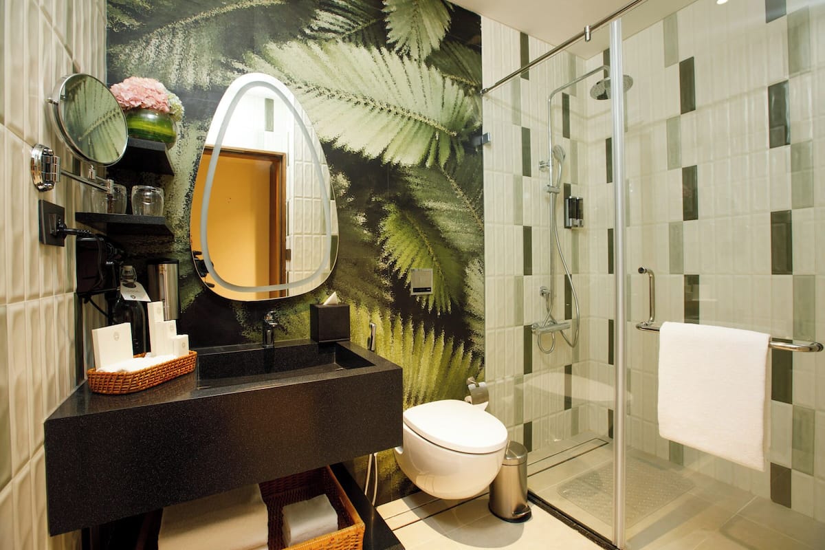 Un baño moderno con cabina de ducha de vidrio, tocador negro con espejo y un inodoro blanco.