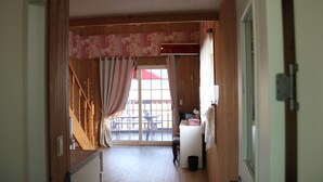 Un pasillo interior de madera que conduce a un balcón con mesa y sillas, un escritorio pequeño con una computadora y un cubo de basura.