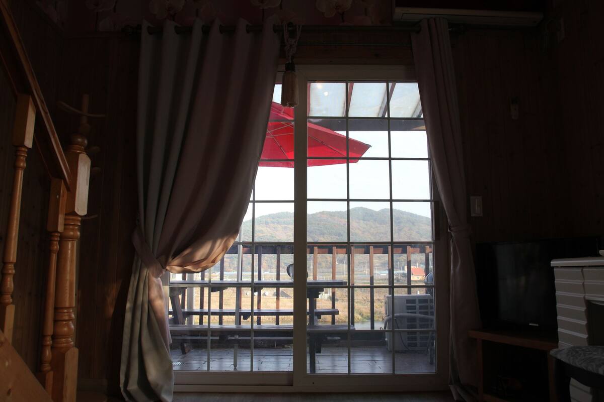 Una stanza con una scala in legno, una televisione e un balcone con un ombrellone rosso.