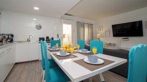 Une cuisine moderne avec des meubles blancs, une table à manger entourée de chaises bleues et un téléviseur à écran plat fixé au mur.