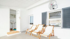 Une pièce comprenant trois fauteuils en bois, un ventilateur de plafond, une fenêtre avec des stores et une vue sur l’extérieur.