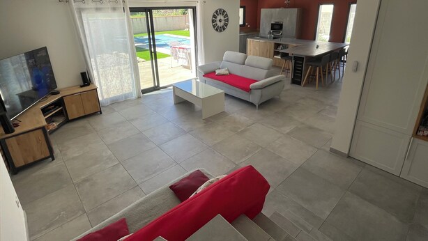 A modern living room with a flat-screen TV, a sofa, and a dining area with a kitchen in the background. - Villa chat l'heureuse (Villemolaque)