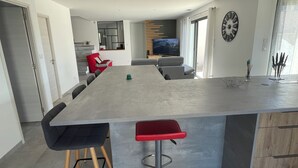 A modern kitchen with a large island, grey chairs, and a red stool. - Villa chat l'heureuse (Villemolaque)