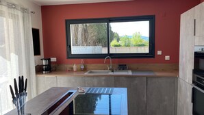 A modern kitchen with a large window, a built-in sink, and a sleek countertop. - Villa chat l'heureuse (Villemolaque)