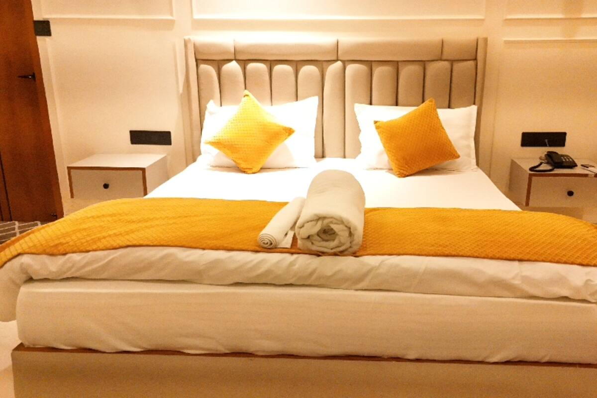 A neatly made bed with a white and yellow bedspread, two pillows, and a rolled towel.