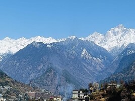 A mountainous landscape with snow-capped peaks and a small settlement with buildings.