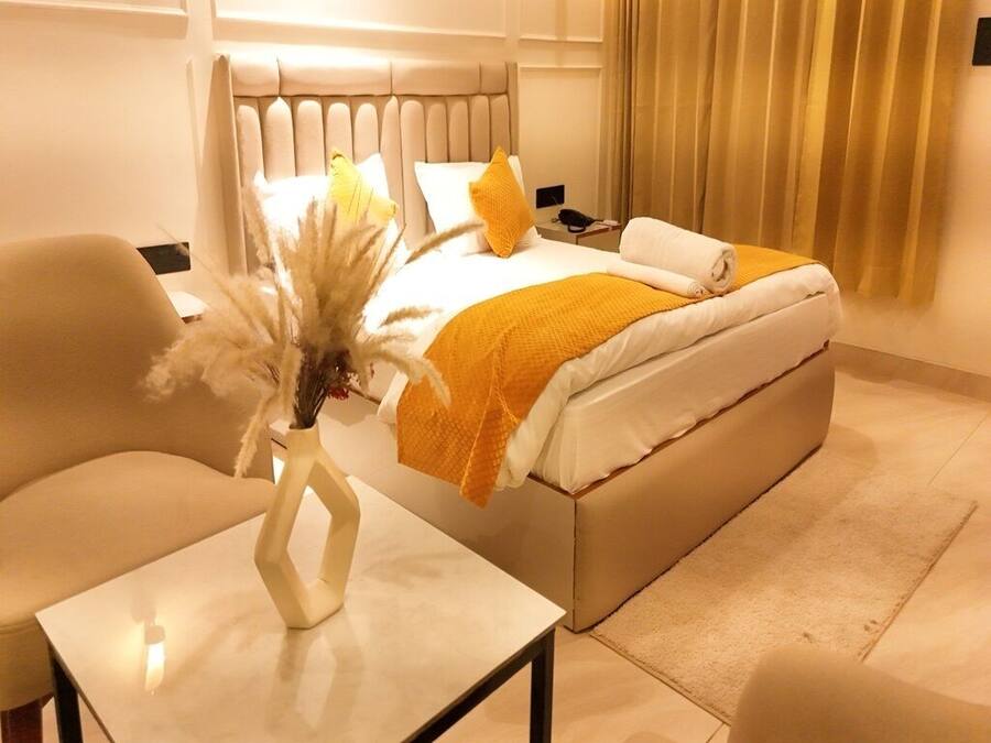 Una habitación de hotel con una cama, una mesita de noche, una silla y un jarrón con flores secas.