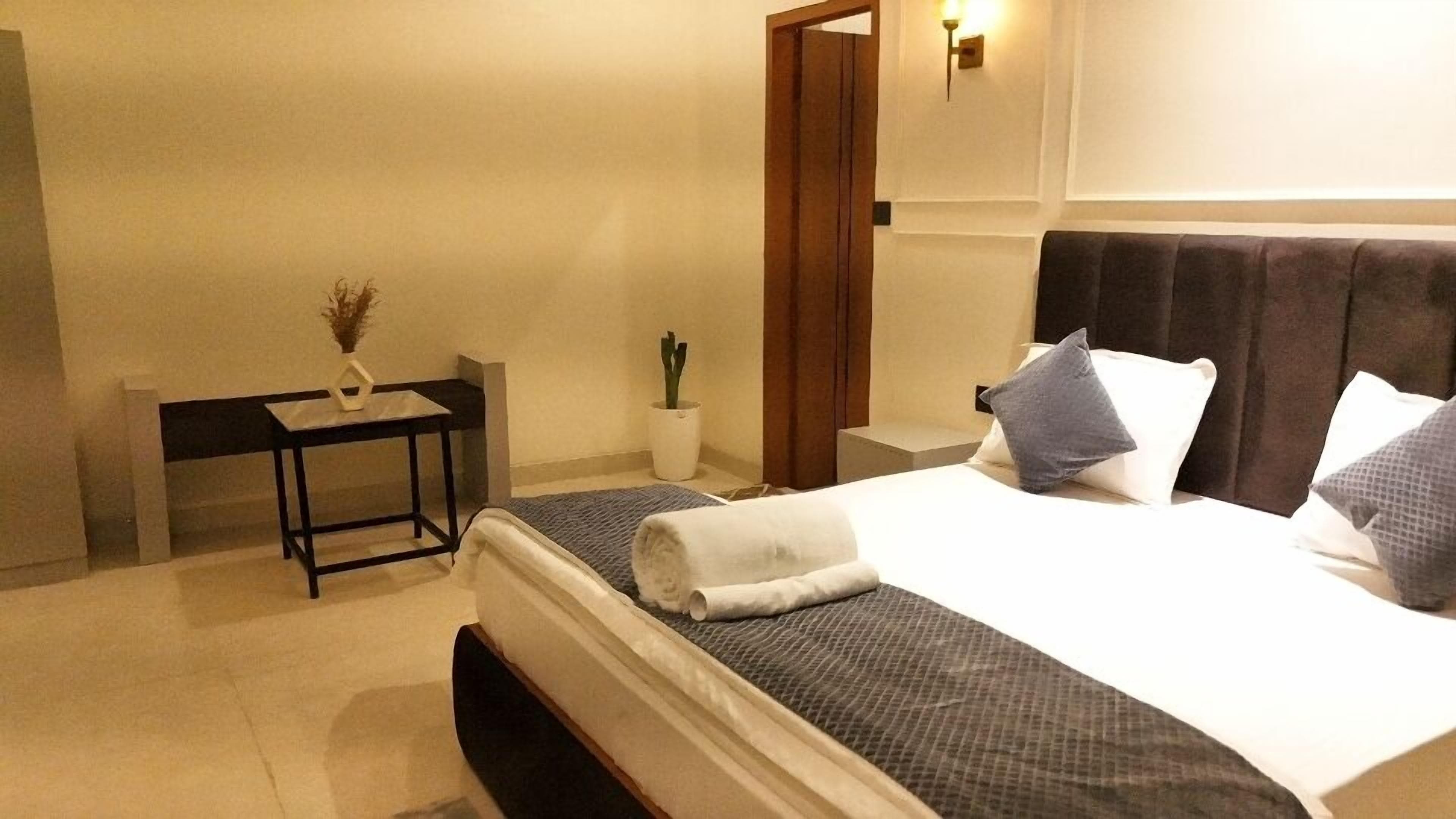 A hotel room with a bed, bedside table, and a small potted plant.