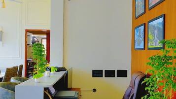 Un salón de conferencias con una mesa de madera, sillas, un escritorio con una computadora y una planta en maceta.