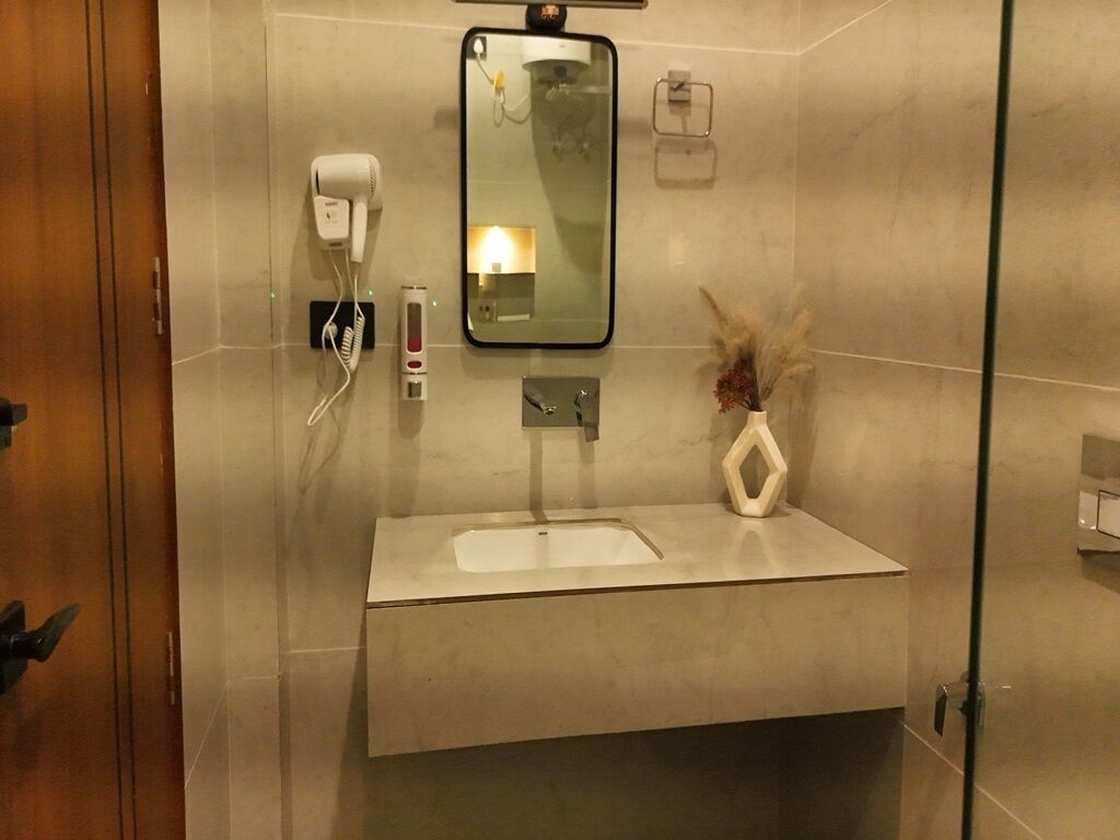 Un baño moderno con un espejo grande, un lavamanos integrado, un secador de pelo y un jarrón con flores secas.