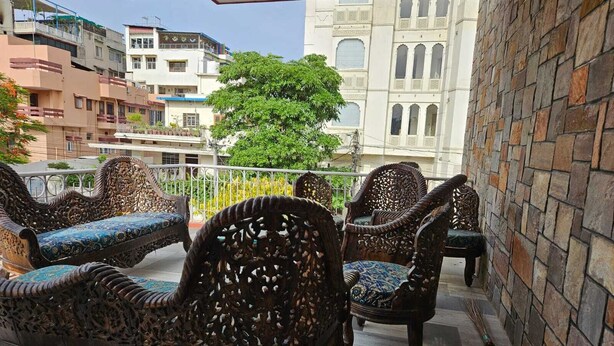 Un balcon agrémenté de meubles en osier décoratifs, avec vue sur des immeubles et un arbre.