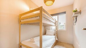 Ett rum med en våningssäng, ett fönster, en hängande lampa och en liten hylla med en växt.