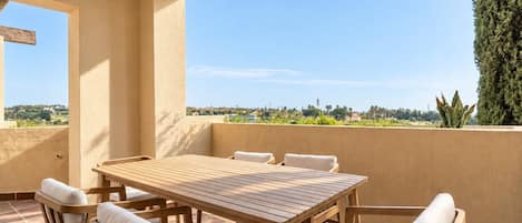 A wooden table with six chairs on a balcony with a view of a landscape.