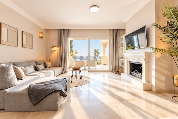 A modern living room with a sofa, a television, a fireplace, and a balcony with outdoor furniture.